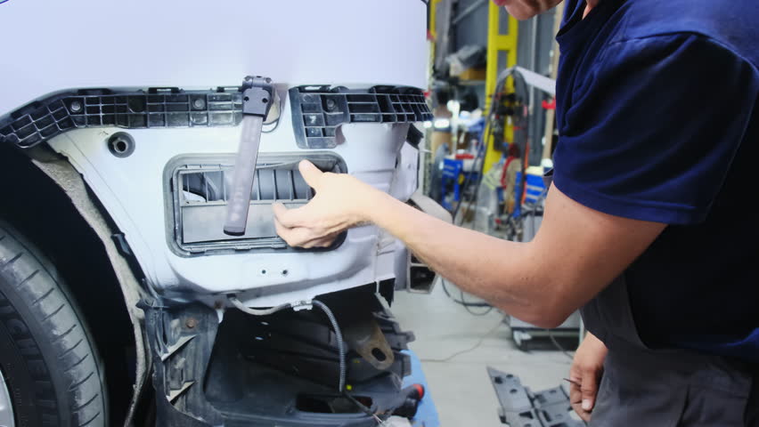 Mechanic hand takes off grid to access car body details in repair shop closeup. Worker engages in vehicle casing restoration at service station