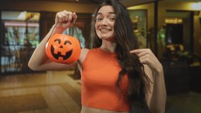 Woman holds halloween pumpkin bucket and points finger to object in brightly lit hotel lobby; excitement. - Powered by Shutterstock - Get 15% off with code: PIKWIZARD15