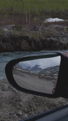 Rear view mirror reflecting northern countryside with river and rural road, autumn. Beautiful fall from window of automobile. Explore Northern nature. Tourism in the North. Scandinavian landscape