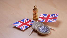 Miniature Big Ben, Union Jack flags, and pound coins symbolizing the United Kingdom's economic crisis, structural stagnation, fiscal imbalance, and the challenges of global inflation - Powered by Shutterstock - Get 15% off with code: PIKWIZARD15