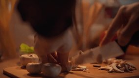 In a warm kitchen, a person skillfully slices fresh mushrooms on a wooden cutting board. Person slicing mushrooms in a cozy kitchen preparation scene during evening cooking time - Powered by Shutterstock - Get 15% off with code: PIKWIZARD15