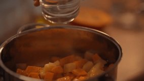 A hand pours water into a pot filled with diced pumpkin in a warm kitchen. The scene captures the process of making creamy pumpkin soup, showcasing a comforting culinary experience - Powered by Shutterstock - Get 15% off with code: PIKWIZARD15
