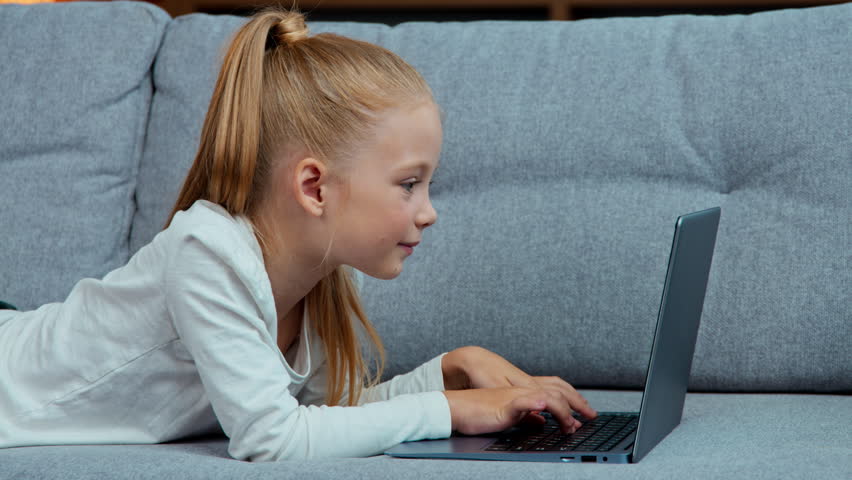 Caucasian little girl child using laptop lying on couch at home kid daughter browsing typing computer websites on sofa playing video game enjoying internet online e-learning children tech addiction - Powered by Shutterstock - Get 15% off with code: PIKWIZARD15