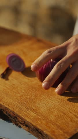 A person is cutting an onion on a wooden cutting board. The onion is being sliced into thin pieces