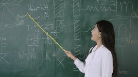 Back to school in summer. Happy Asian young female math teacher standing holding a pointer and teaching a mathematics lesson on chalkboard in front of the classroom, Concept of learning and education. - Powered by Shutterstock - Get 15% off with code: PIKWIZARD15