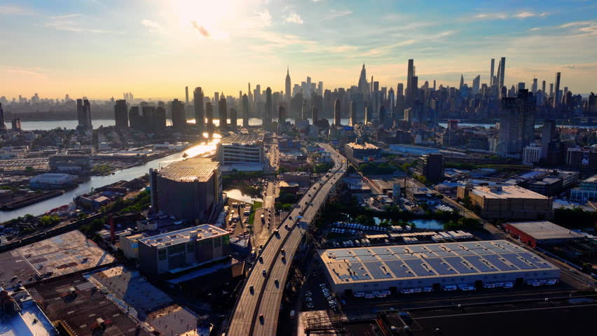 Sunset view of Manhattan skyline from Queens with roads and warehouses. Aerial view, panorama of New York City with blue sky.