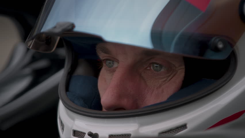 Close-up of a focused pilot driver in a red racing car, wearing a helmet, preparing for a high-speed race