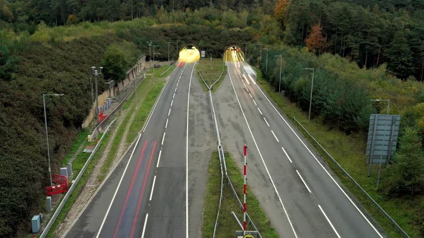 Timelapse showing light trails from vehicles driving on a highway entering two tunnels as the day transitions from sunset to night