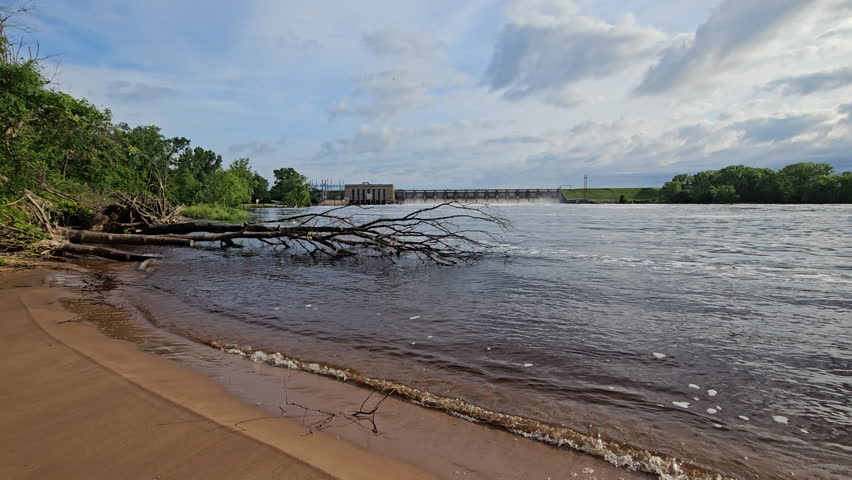 Wide angle distant view from beach at hydroelectricity dam with all spillways partially opened after heavy rains raised Wisconsin Rive level.