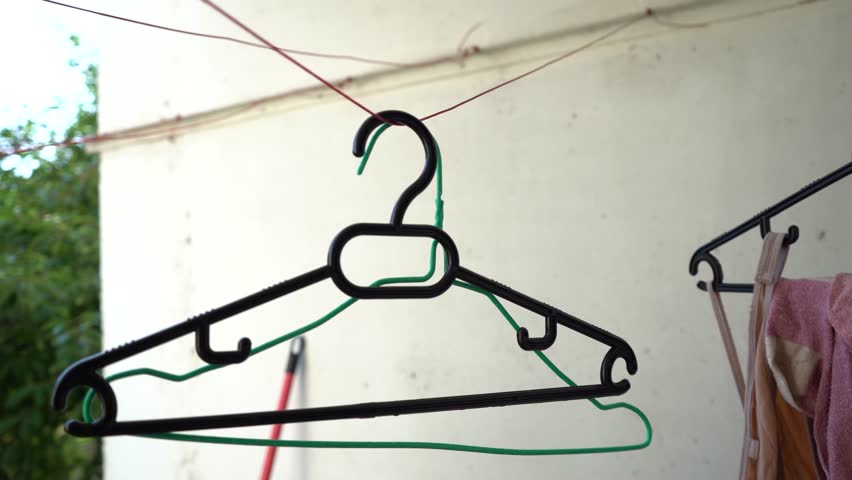 A woman arranging empty hangers on a clothesline outdoors.