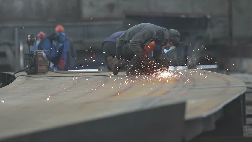 A worker grinds a metal plate or sheet with a hand grinder. Worker Grinding Metal Plate. Steel structure metalworking shop. Worker preparation steel plate by hand grinding machine.