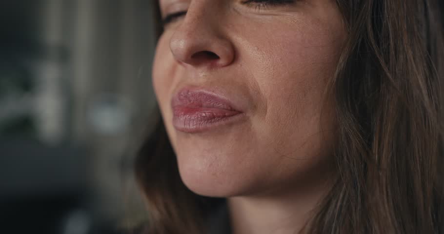 Close-up of woman in office setting eating a pastry highlighting mouth and fingers holding the sweet treat with blurred background