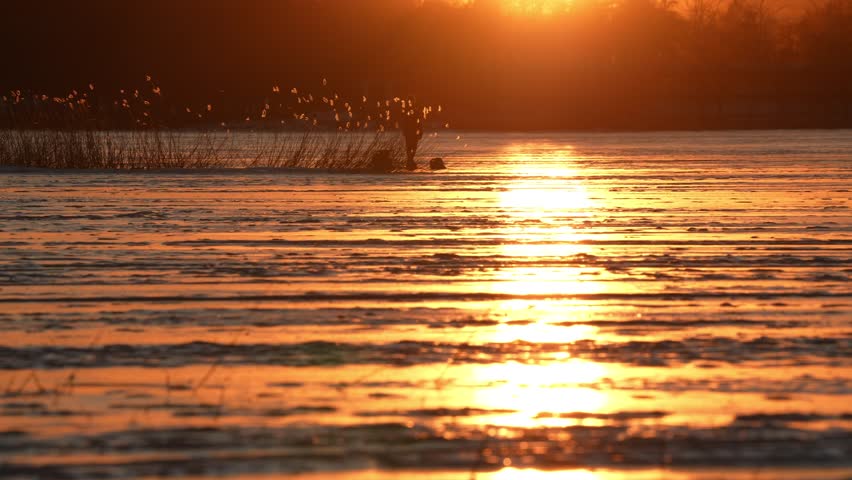 Beautiful sunset over ice-covered lake with patches of snow and scattered hay, capturing the simplicity of Finnish nature.