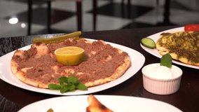 A table featuring various Lebanese flatbreads topped with different ingredients, including a spread of minced beef. The dishes are garnished with fresh herbs and served with fresh vegetables. - Powered by Shutterstock - Get 15% off with code: PIKWIZARD15