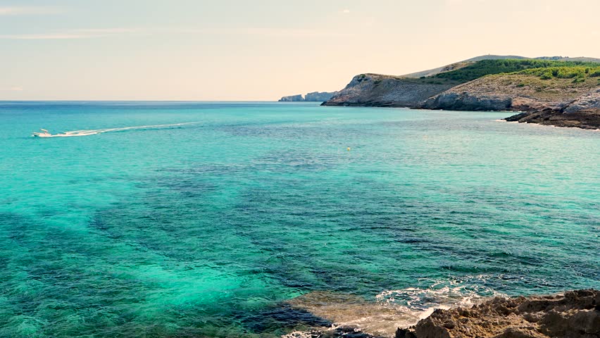 Small motorboat glides across turquoise Mediterranean Sea near Cala Torta beach, Mallorca. Peaceful seascape, perfect for travel, relaxation themes