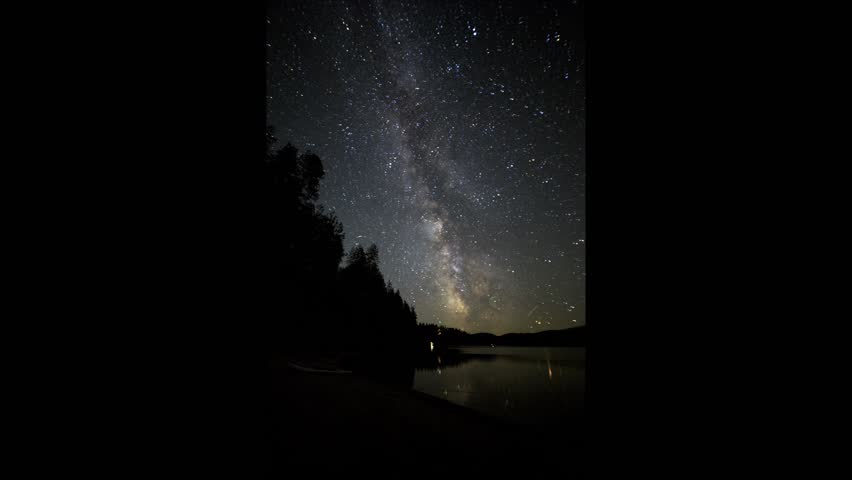 Star trails arc across the night sky in a long-exposure timelapse above Lake Roosevelt, part of the Columbia River near Kettle Falls, WA, reflecting bright starlight on the tranquil water and forested