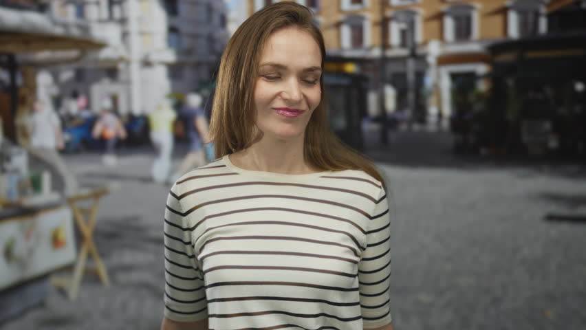Woman in striped shirt flexes arm on a cobblestone street in a historic city square during daylight hours; confidence empowerment.
