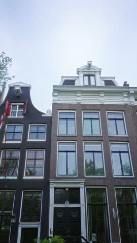 European architecture in amsterdam showcasing historic brick building facade with tall windows and lush green tree against a clear sky.