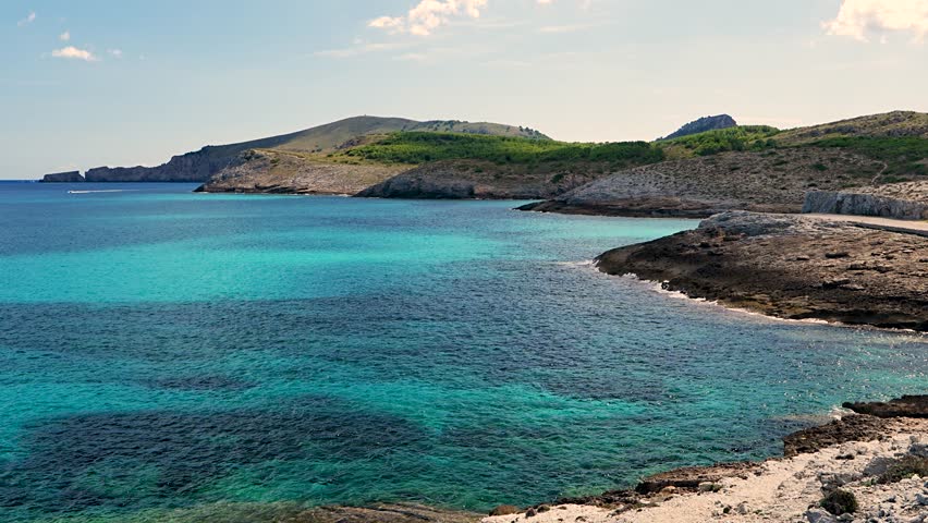 Motorboat cruising on clear turquoise sea with vibrant color gradients and rocky coastline. Stunning Mediterranean scenery near Cala Torta, Mallorca, Spain.