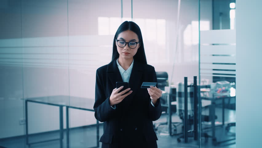 Millennial manager checks mobile and credit card in modern office setting