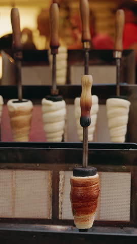 Fresh Czech Trdelnik pastry baking on wooden rollers in a street market stall in Prague, golden brown and ready to serve. High quality 4k footage