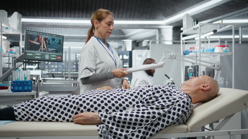 Magnifying glass used by medic monitoring a senior man for clinical trial in laboratory, checking the skin of the patient. Female expert working in lab for medical breakthrough. Camera A.