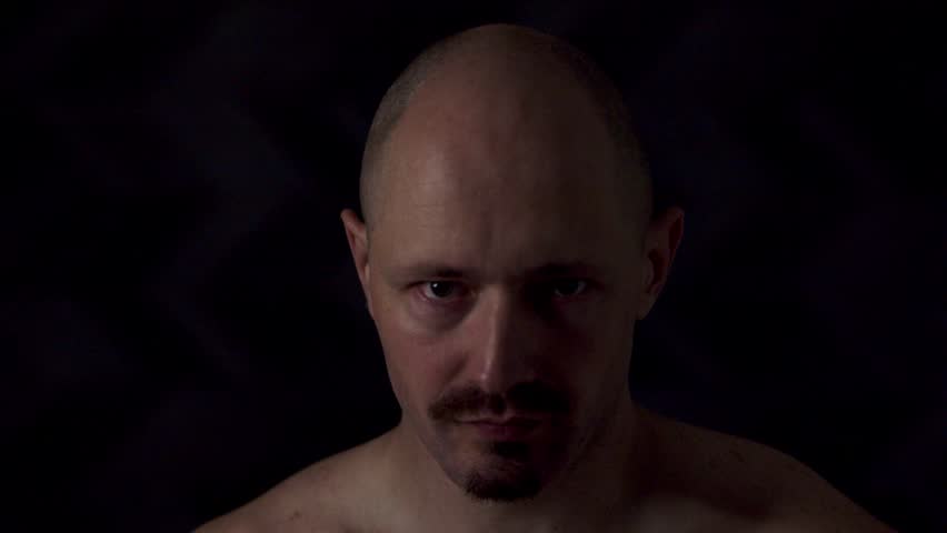 Close-up portrait of an athletic man against a dark background. He moves his head quickly from side to side, causing his mouth and cheeks to tremble.
