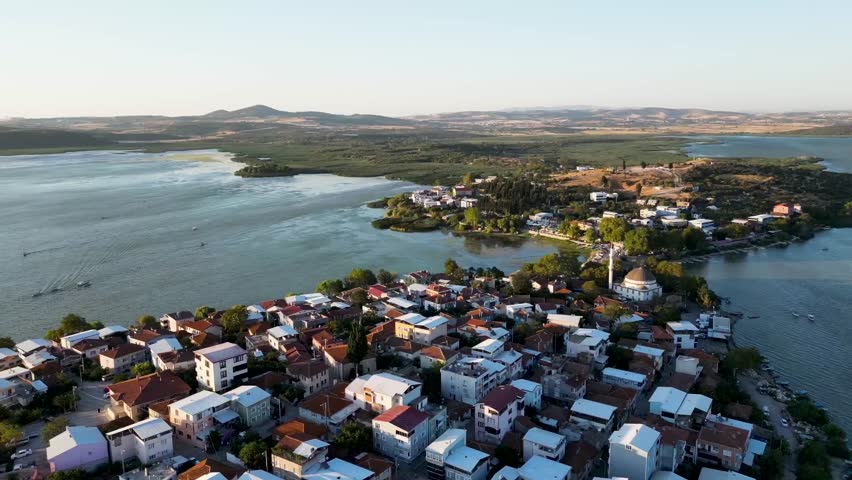 Aerial view of town beside blue water surrounded by green hills.