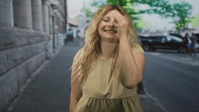 Blonde woman smiling with hand to forehead, head tilted and laughing while standing on a cobblestone city street; joy laughter smile. - Powered by Shutterstock - Get 15% off with code: PIKWIZARD15