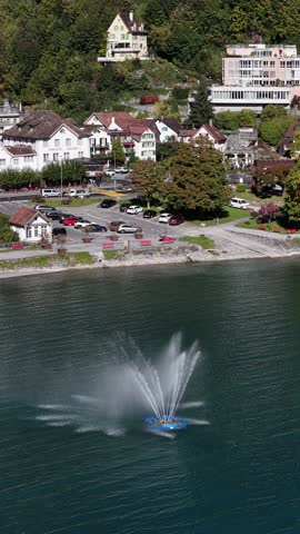 Vertical aerial view of a water fountain spraying on Lake Walensee in Walenstadt, Switzerland, with charming alpine houses and scenic lakeside surroundings, concept of travel and serenity.