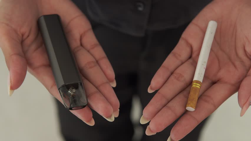Close up of an Asian woman presenting a stick of cigarette and a vape electric cigarette.