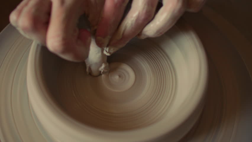 Hands of artisan working on inner surface of clay bowl on spinning pottery wheel during ceramic making process. Close-up view