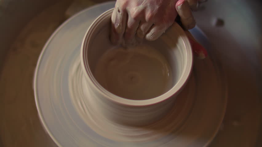 Close-up of hands smoothing inner surface of clay bowl on spinning pottery wheel during ceramics shaping process in art studio