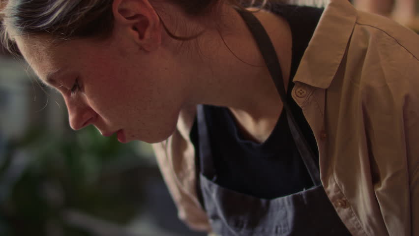 Young female ceramics artist forming clay vessel by hand on spinning pottery wheel during crafting process in workshop. Close-up, tilt down shot