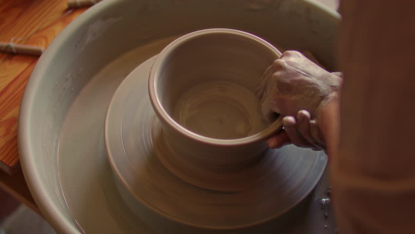 Hands of female artisan shaping clay into rounded bowl on spinning pottery wheel in ceramics studio. Close-up view