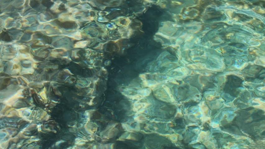 Crystal clear sea water rippling over a rocky seabed in bright sunshine, creating abstract patterns