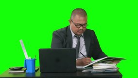 Businessman analyzing documents and writing notes at office desk with laptop, isolated on green screen - Powered by Shutterstock - Get 15% off with code: PIKWIZARD15