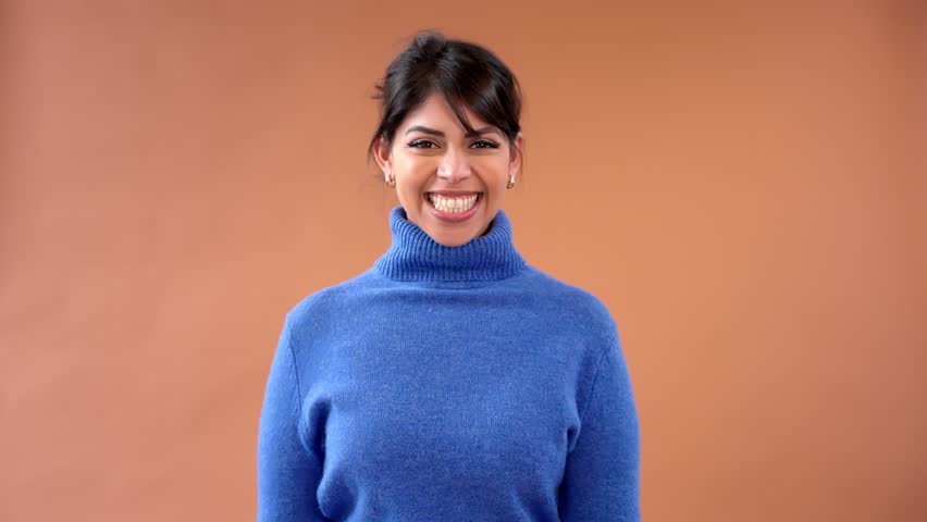 Smiling woman with blue sweater shows hand greeting in a cozy indoor space