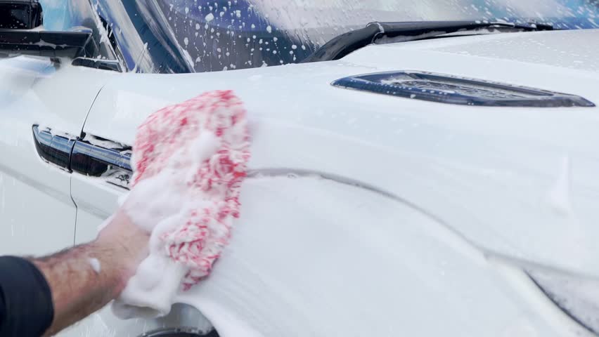 Close up cleaning white SUV with red microfibre wash mitt and lots of suds