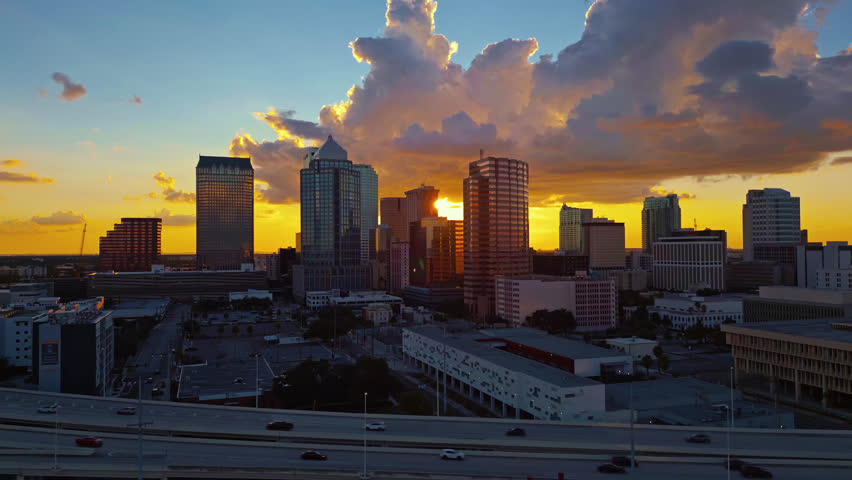 Aerial rising shot of downtown Tampa city skyline during the golden hour sunset with glowing clouds.