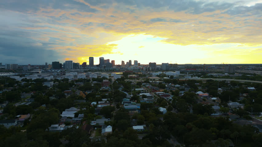Aerial sunrise or sunset golden hour establishing shot over a small neighborhood near downtown Tampa with glowing clouds and skyscrapers in the background.