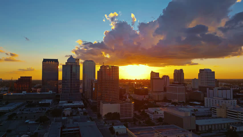 Stunning aerial tracking shot of the Tampa, Florida skyline during a beautiful golden sunset. The camera moves left, with the downtown skyscrapers backlight by the evening sunlight.