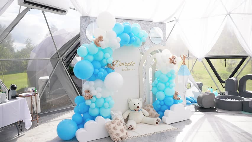 Beautiful blue and white baptism decoration setup for a baby boy inside a dome tent, featuring balloons, teddy bears, soft pillows, and a personalized name display.