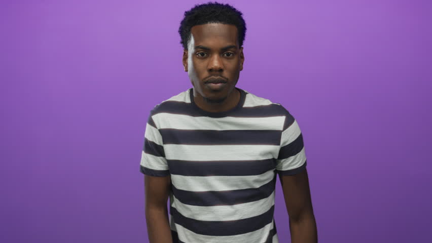 Man pinches thumb and index finger close together in a purple studio setting; precision contemplation.