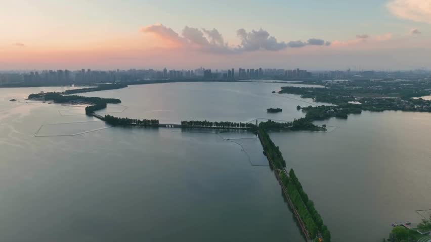 Scenic aerial view of a modern city skyline across a tranquil lake at sunset. A beautiful cityscape with a causeway reflecting in the calm water.
