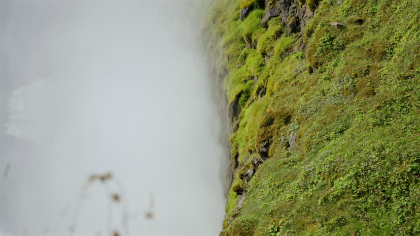 Green mossy rocks near powerful waterfall mist