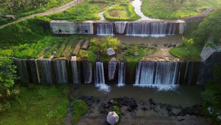 Aerial view of the tiered Watu Purbo Waterfall cascading down concrete steps amidst lush greenery, creating a stunning visual contrast, Sleman, Yogyakarta, Indonesia.