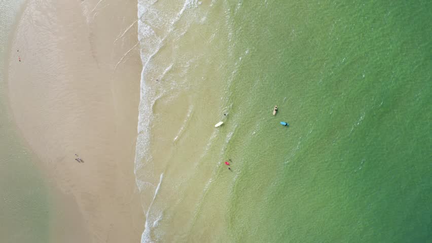 Aerial view of the beach with people enjoying the waves and surfboards floating on the water, Newquay, England, United Kingdom.