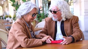 Elderly man giving red gift box to surprised senior woman at outdoor cafe terrace. Happy couple celebrating special moment, love,affection, birthday,anniversary, retirement, emotion, joy, togetherness - Powered by Shutterstock - Get 15% off with code: PIKWIZARD15