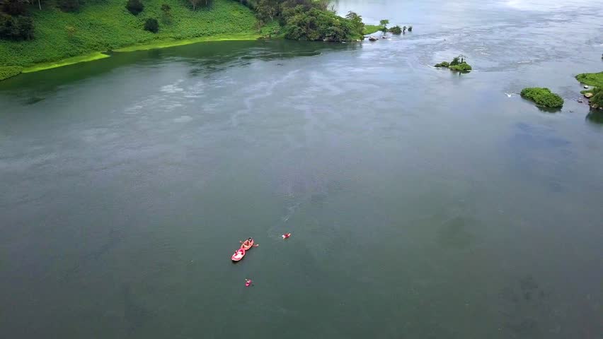 Drone view of white water rafting on the River Nile in Uganda, showing red rafts, lush riverbanks, and scenic water channels near Jinja.